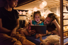 Family With Tablet On Small Bed In Lights
