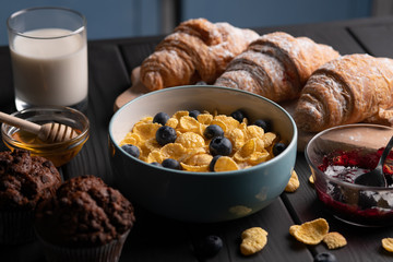 Muffin, croissant and bowl corn flakes. Sweet food. Healthy delicious meal. Black background. Kitchen.