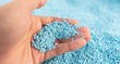 Hand on large pile of blue plastic granules in temporary storage of production line at recycle factory, masterbatch dye polymer plastics resin pellet background,  injection molding process lab