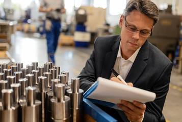 Wall Mural - Manager writing reports while performing quality control check in a steel factory.