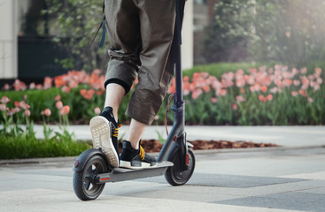 Wall Mural - Close up of man riding black electric kick scooter at beautiful park landscape