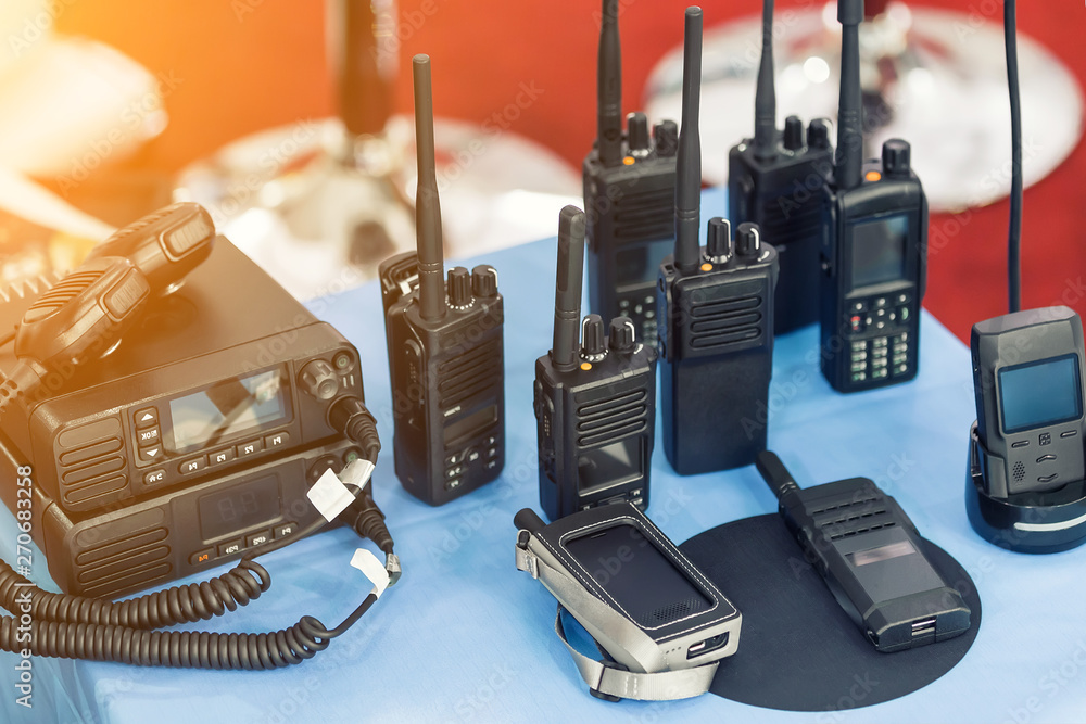 Many portable radio transceivers on table at technology exhibition. Different walkie-talkie radio set. Communication devices choice for military and civil use - obrazy, fototapety, plakaty 