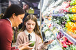 © Maskot - Mother showing cucumber to daughter while grocery shopping in supermarket