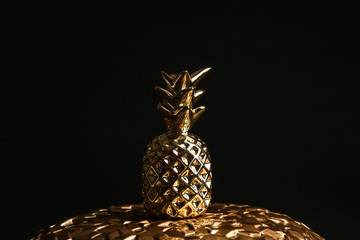 Gold decorative pineapple on plate against black background