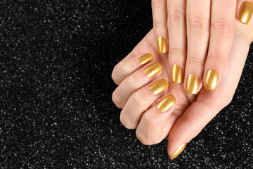 Wall Mural - Woman showing manicured hands with golden nail polish on black background, closeup. Space for text