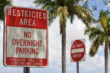 Restricted Area No Overnight Parking Sign. Red And White Warning Sign And DoNot Enter Sign, With Palm Trees And Partly Cloudy Sky In Backgroun