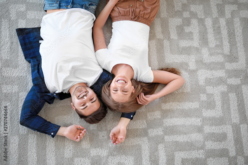 Young couple lying on soft carpet at home, top view