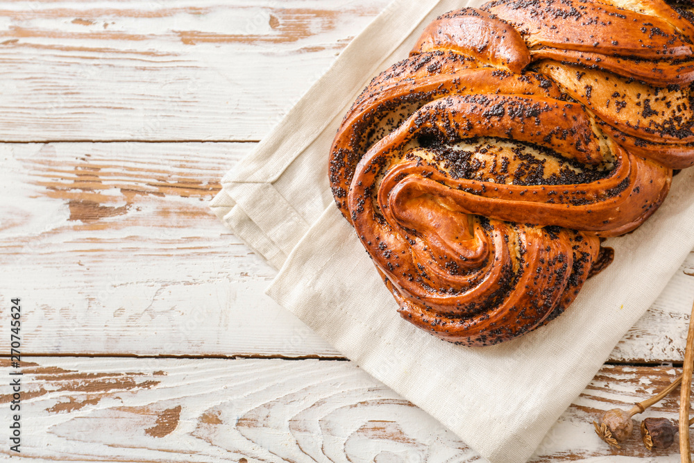 Tasty bun with poppy seeds on wooden table