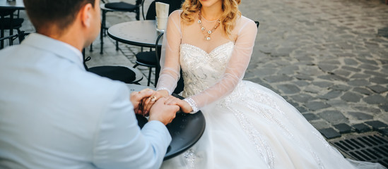 Wall Mural - Bride and groom sitting in the old town street cafe. Wedding couple in love. Luxury rhinestone dress. Hot summer days.