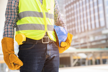 Close up backside view of engineering male construction worker stand holding safety white helmet and wear reflective clothing for the safety of the work operation. outdoor of building background.