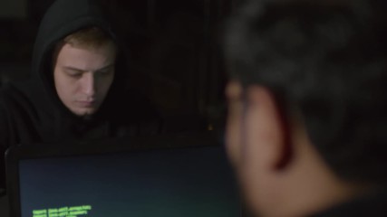 Wall Mural - rare view of two male hackers sitting at table in darkness, typing and getting access to databank