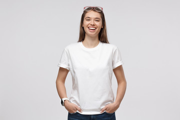 Young girl standing with hands in pockets, wearing blank white t-shirt with copy space, isolated on gray background