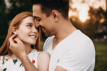 Wall Mural - Side view portrait of a beautiful young couple smiling while looking to each other while man is touching her girlfriends face against sunset .