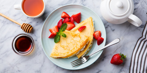 Wall Mural - Crepes, thin pancakes with cream cheese, ricotta and fresh strawberries. Marble background. Top view.