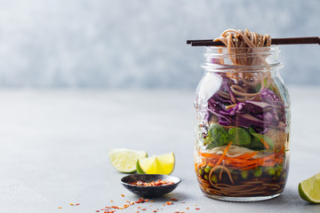 Healthy asian salad with noodles, vegetables, chicken and tofu in glass jars. Grey background. Copy space.