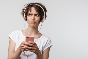 Canvas Print - Image of upset woman in basic t-shirt holding smartphone while listening to music with headphones