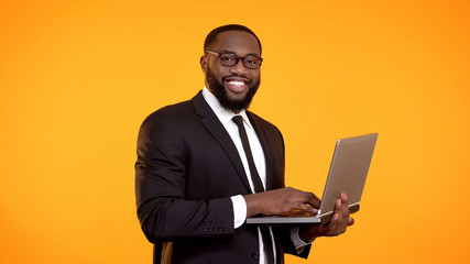 Wall Mural - Smiling afro-american businessman working on laptop, career growth, business