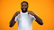 © motortion - Smiling black man showing his white T-shirt isolated on yellow background