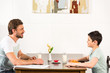 © LIGHTFIELD STUDIOS - father and son looking at each other during breakfast in kitchen