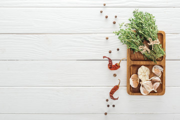 top view of dried chili peppers, black pepper near board with garlic cloves and thyme on white wooden table