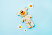 Amigurumi Handmade Teddy Bear With Daisies Isolated On A Blue Background. Baby Background. Copy Space, Top View.