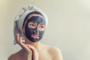 Wall Mural - Beauty portrait of woman in towel on head applying black nourishing mask on face, white background isolated. Skincare cleansing eco organic cosmetic spa relax concept