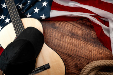 Fototapete - American culture, cowboy living on a ranch and country muisc concept theme with a black baseball cap, USA flag, rope lasso and acoustic guitar on a wooden background in a old saloon with copy space