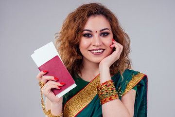 Wall Mural - indian beautiful fashion brunette woman in green traditional wedding rich sari with gold jewelry set nose ring piercing nath professional make-up on white studio background bindi holding a passport 