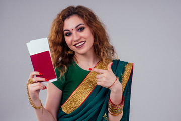 Wall Mural - indian beautiful fashion brunette woman in green traditional wedding rich sari with gold jewelry set professional make-up on white studio background bindi holding a passport and boarding passes