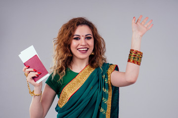 Wall Mural - indian beautiful fashion brunette woman in green traditional wedding rich sari with gold jewelry set professional make-up on white studio background bindi holding a passport and boarding passes