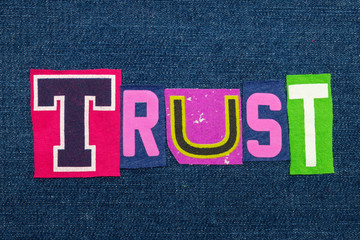 TRUST text word collage in brightly colored fabric on blue denim, confidence and fidelity, horizontal aspect