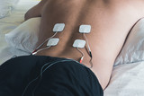 Fototapeta Zachód słońca - Patient applying electrical stimulation therapy on back. Electrical tens.