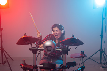 Electronic drum set, music and hobby concept - young woman drummer playing in headphones