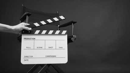 Hand is holding white Clapper board or movie slate with director chair use in video production or movie and cinema industry. It's on black background.