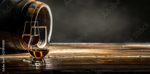 Fotografía Two glasses of whiskey standing against an oak barrel