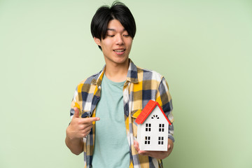 Asian man over isolated green wall holding a little house