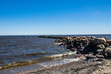 lonely empty sea beach with white sand, large rocks and old wooden trunks on the shore