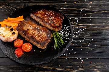 Wall Mural - juicy piece of fried meat lies on a stone plate against a black wooden table