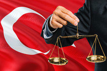 Turkish Judge Is Holding Golden Scales Of Justice With Turkey Waving Flag Background. Equality Theme And Legal Concept.