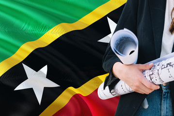 Architect woman holding blueprint against Saint Kitts And Nevis waving flag background. Construction and architecture concept.