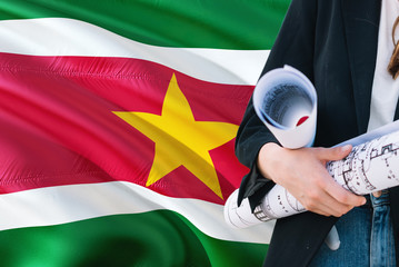 Surinamese Architect woman holding blueprint against Suriname waving flag background. Construction and architecture concept.