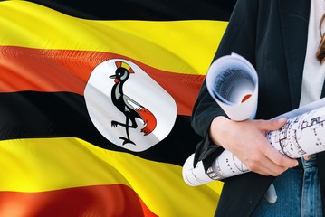 Ugandan Architect woman holding blueprint against Uganda waving flag background. Construction and architecture concept.