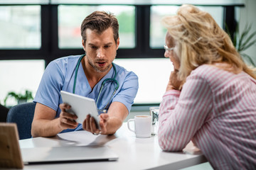 Wall Mural - Serious doctor and his female patient using touchpad during medical appointment.