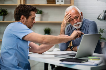 Wall Mural - Worried senior patient and his doctor looking at medical results on laptop.