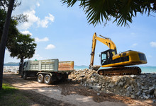Excavator Digger Stone And Dump Truck Working On Construction Site / Backhoe Loader On The Beach Sea Ocean