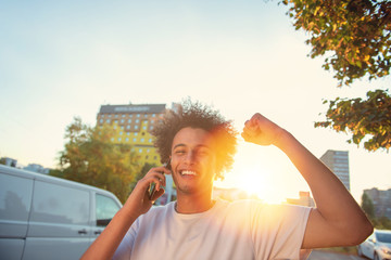 happy smiling urban hipster young man using smart phone. African american teenager holding mobile smartphone on sunset with lens flare
