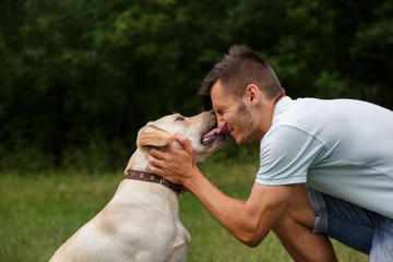 Friendship and love of man and dog. Happy young man kissing with his friend - dog Labrador