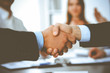 © rogerphoto - Business people shaking hands at meeting while theirs colleagues clapping and applauding. Group of unknown businessmen and women in modern white office. Success teamwork, partnership and handshake
