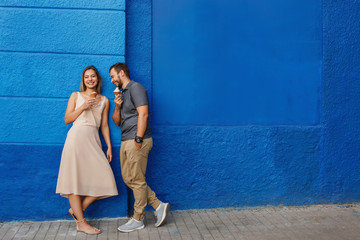 Happy couple having fun, eating ice cream and smiling against the blue wall