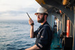 Deck Officer on deck of offshore vessel or ship , wearing PPE personal protective equipment. He holds VHF walkie-talkie radio in hands. Dream work at sea
